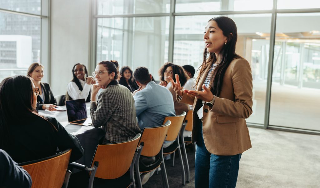 A confident female leader engages a diverse team in a professional workshop, promoting teamwork and fresh ideas in a bright office environment.