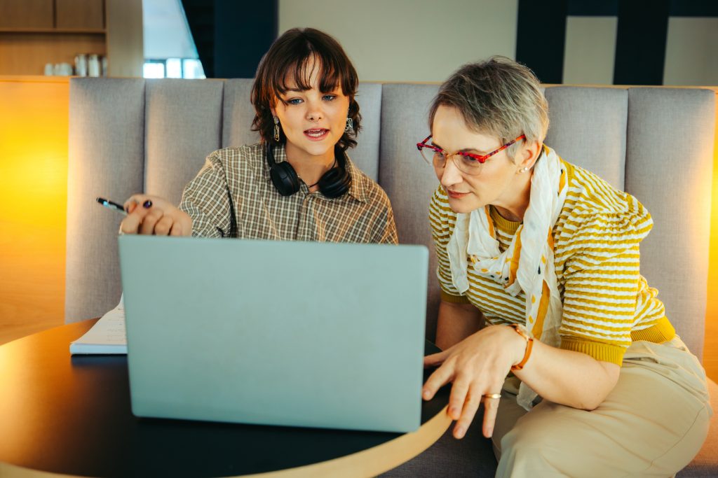 Two colleagues of different ages collaborating on a project using a laptop, showcasing diversity and teamwork in a professional environment.