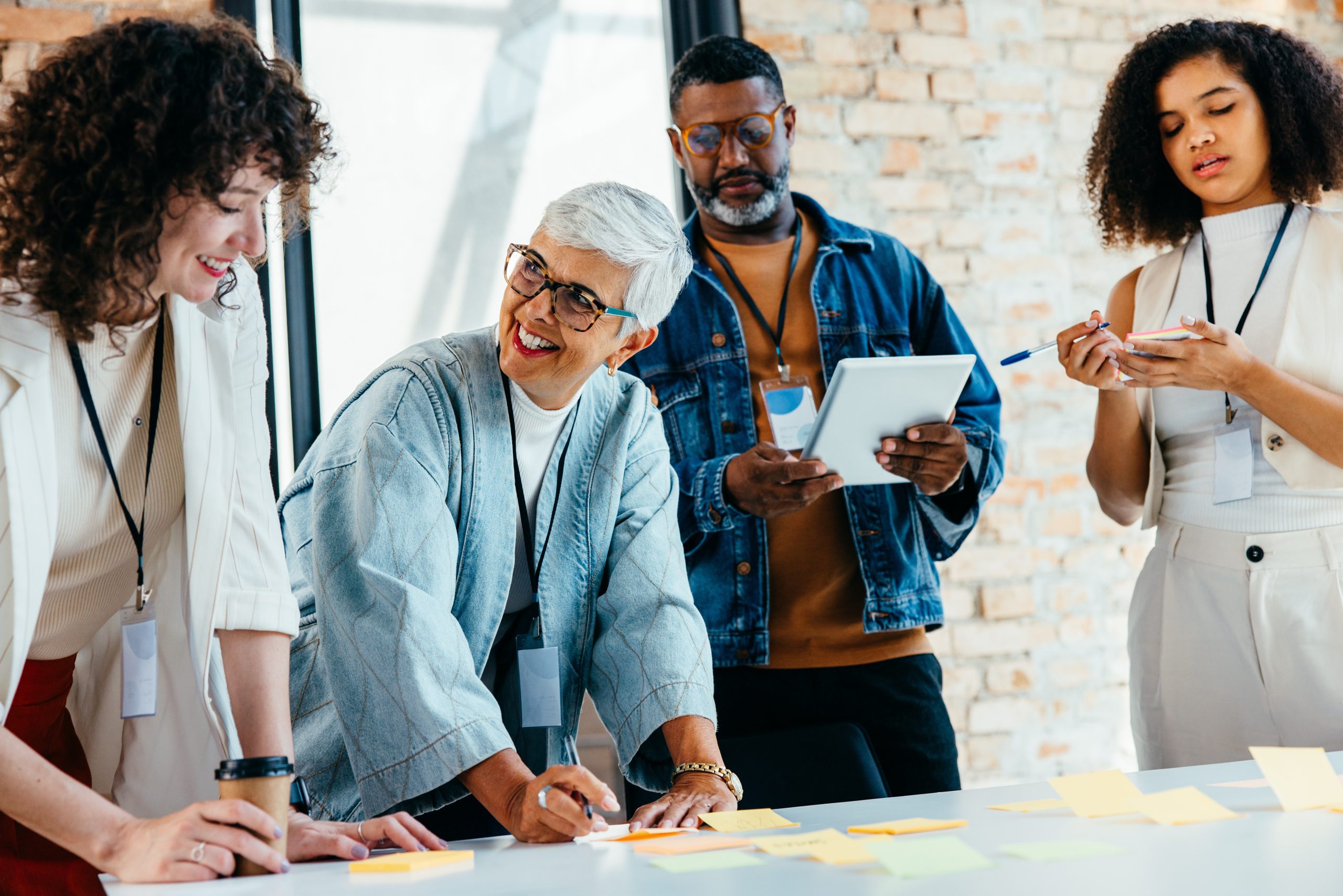 A diverse team of professionals brainstorms in a modern office, using post-it notes and digital tablets for collaborative project planning and creative discussion.